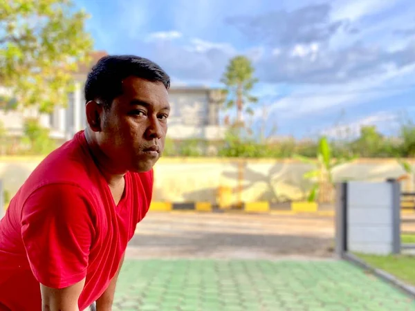 The young man in the red shirt squats in the yard