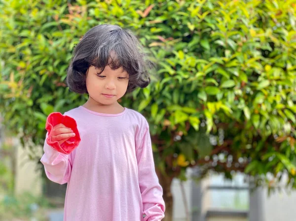 Pembe elbiseli ve yeşil yapraklı gülümseyen küçük bir kızın portresi.