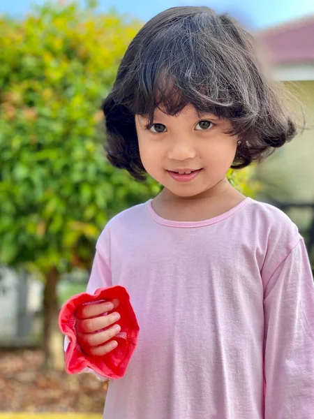 Pembe elbiseli ve yeşil yapraklı gülümseyen küçük bir kızın portresi.