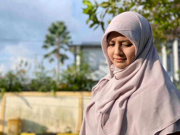 Başörtüsü takan genç, güzel bir kadın ve yüzünde mutlu bir ifadeyle kameraya gülümsüyor.