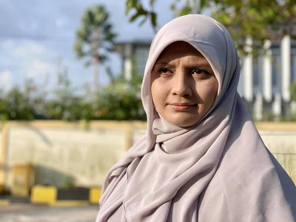 Başörtüsü takan genç, güzel bir kadın ve yüzünde mutlu bir ifadeyle kameraya gülümsüyor.