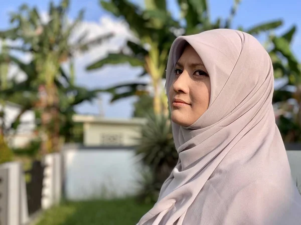 Başörtüsü takan genç, güzel bir kadın ve yüzünde mutlu bir ifadeyle kameraya gülümsüyor.