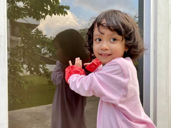 Portrait of a little girl wearing a pink dress, in front of a glass wall of a building