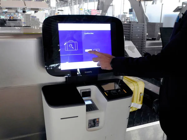A hand pressing on the monitor, Self check-in machine at the airport, loading baggage, self bag drop and getting the boarding pass.
