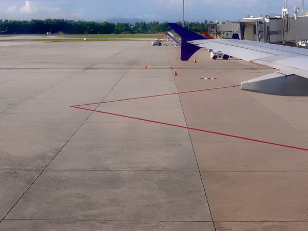 Airplane wing with docked ladder at the airport field apron, taxiway with red line marking