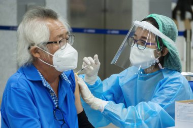 Bangkok, Tayland - 16 Ocak 2022: Asyalı doktor veya hemşire Bang Sue Grand Station 'da Coronavirus' tan koruyucu yüz maskesi takan yaşlı bir hastaya covid antivirüs aşısı yapıyor..
