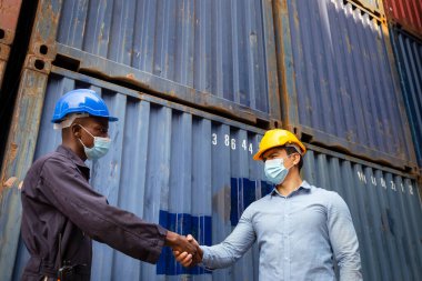 Afrikalı işçi ve Kafkasyalı işadamı Covid veya Coronavirus 'u korumak için yüz maskesi takıyor. Kargo deposunda başarılı lojistik ve ulaşım hizmetlerinin ardından el sıkışıyorlar..