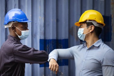 Rıhtımdaki kargo deposundaki kovid veya koronavirüsten korumak için yüz maskesi takan Afrikalı mühendis ve Kafkas işadamı, şiddetli enfeksiyonu önlemek için selamlaşıp dirseğe dokunuyorlar.. 