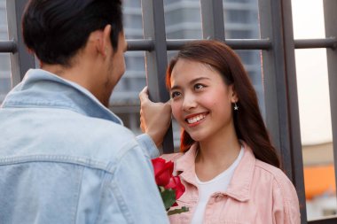 Genç mutlu çift ilk buluşmada aşk ve romantizm yaşar. Asyalı genç bir kadın sevgilisine sürpriz yapar ve sevgililer gününde kırmızı gül verir. çift ve mutluluk konsepti.