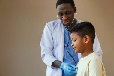 Afro-Amerikan çocuk doktoru. Steteskop kullanarak hastanenin ofisinde küçük bir çocuğu hastalığından tedavi ediyor. tıbbi ve sağlıklı yaşam tarzı konsepti.
