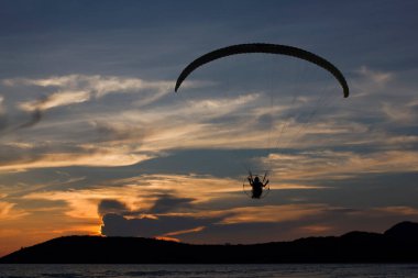 Siluet paraşütçü ya da paraglider güzel bir günbatımı arka planıyla denizin üzerinde uçar..