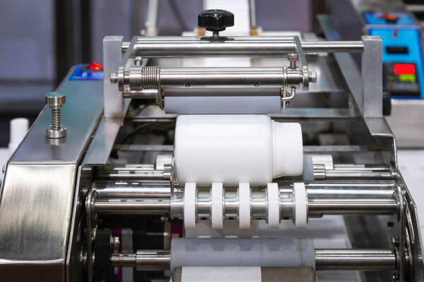 White plastic bottle on small tabletop bottle sticker labeling machine for medicine and pharmaceutical industry.