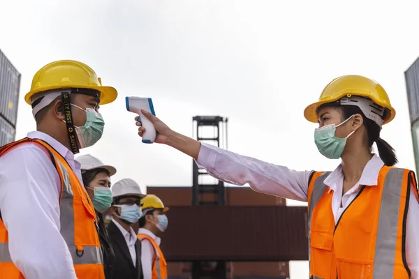 asian man workers wearing face mask checking fever by digital thermometer before entering the work for protecting from covid, covid-19 or coronavirus pandemic on construction site. selective focus.