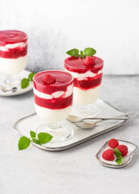 Ev yapımı lezzetli tereyağlı krema ve ahududu soslu tatlı. Taze limon merhemi yapraklarıyla süslenmiş bardaklarda. Sağlıklı gıda konsepti.