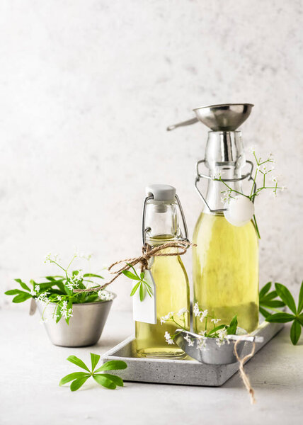 Two glass bottles of homemade sweet woodruff syrup in a grey tray  with fresh green leaves. Healthy summer food concept. Selective focus. Copy space.