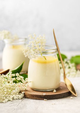 Yaşlı çiçekler panda cotta, limonlu kremalı tatlı cam kavanozlarda hafif bir arka planda. Ev yapımı organik gıda konsepti. Boşluğu kopyala.
