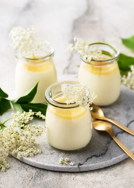 Delicious Italian elder flower dessert, panna cotta with lemon sauce and fresh flowers in portion glass jars. Homemade organic food concept.