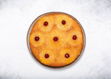 Homemade pineapple upside down cake with glace cherries on a light rustic background. Delicious vegetarian sweet food concept. Horizontal view from above. Copy space.