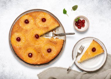 Top view of homemade pineapple upside down cake with candied cherries and a piece cut off on a plate. Summer tropical dessert. 