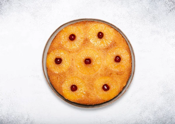 Homemade pineapple upside down cake with glace cherries on a light rustic background. Delicious vegetarian sweet food concept. Horizontal view from above. Copy space.