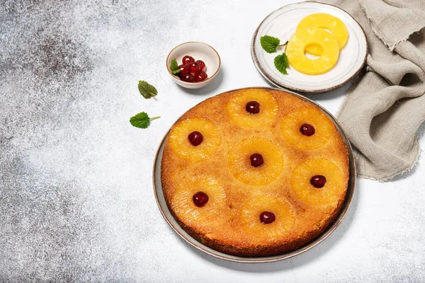 Traditional fresh baked pineapple upside down cake with glace cherries on a light rustic background. Delicious homemade sweet food concept. Selective focus. Copy space.