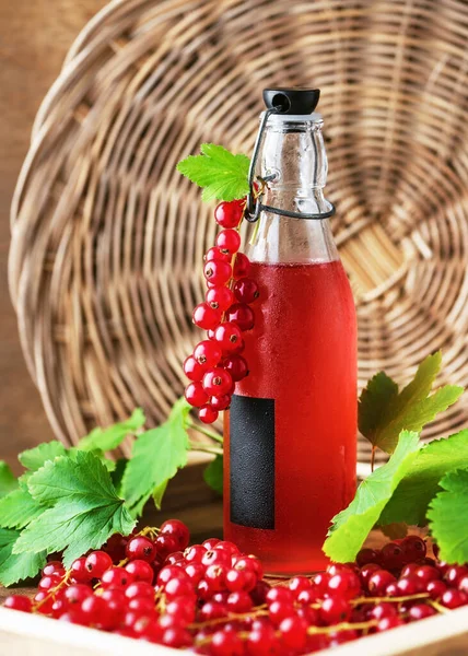 Healthy summer non alcoholic drink of red currant syrup in a glass bottle on a wooden tray with many fresh berries. Healthy homemade food concept. Rustic style.