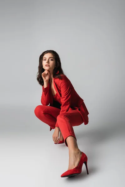 Kırmızı Topuklu Takım Elbiseli Gri Üzerinde Otururken Poz Veren Modaya — Stok fotoğraf