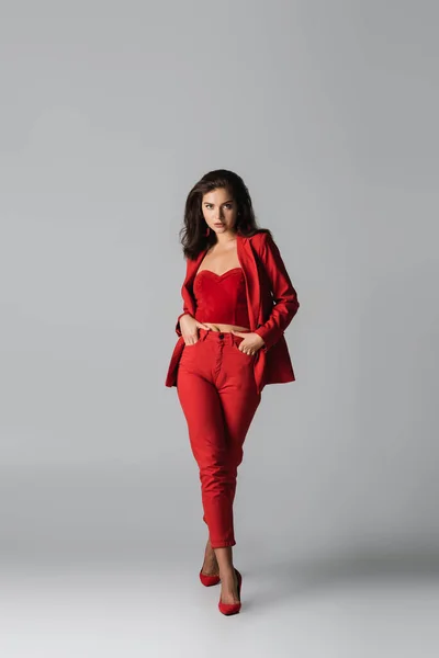 赤かかとの若いスタイリッシュな女性の完全な長さとスーツポークで手でポーズグレー — ストック写真