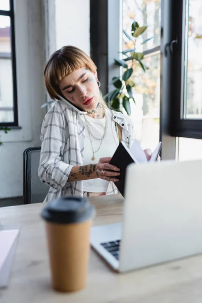 Young Tattooed Businesswoman Holding Notebook While Talking Cellphone Blurred Laptop — Stock Photo, Image