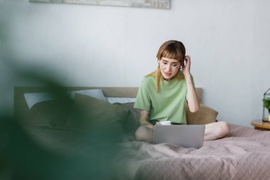 Yatak odasında bulanık ön planda film seyrederken gergin bir kadın kafaya dokunuyor.