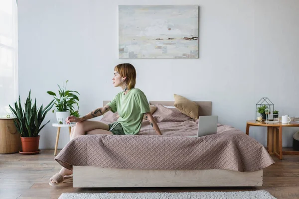 Junge Tätowierte Frau Sitzt Auf Bett Neben Laptop Modernem Schlafzimmer — Stockfoto