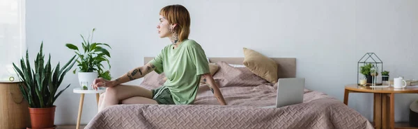 Joven Mujer Tatuada Sentada Cama Cerca Computadora Portátil Dormitorio Moderno —  Fotos de Stock