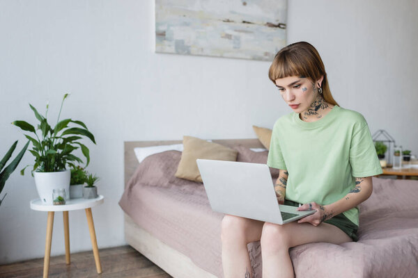 молодая женщина с татуировкой с помощью ноутбука, сидя на кровати дома