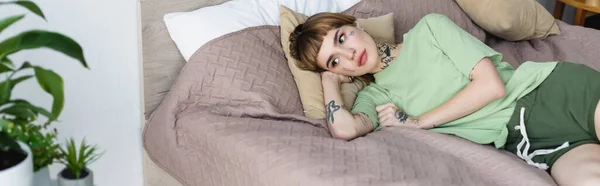 Young Tattooed Woman Lying Bed Blurred Plants Home Banner — Stock Photo, Image