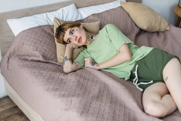 young woman with tattooed body lying on bed at home