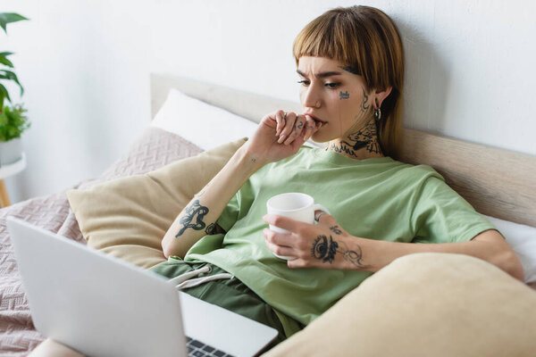 молодая обеспокоенная женщина с татуированным телом смотрит фильм на размытом ноутбуке