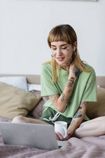 положительная женщина с татуированным телом смотрит фильм на ноутбуке в спальне