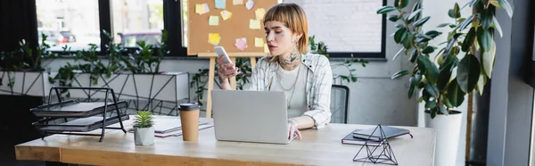 Młoda Stylowa Bizneswoman Pomocą Telefonu Komórkowego Podczas Pracy Pobliżu Laptopa — Zdjęcie stockowe