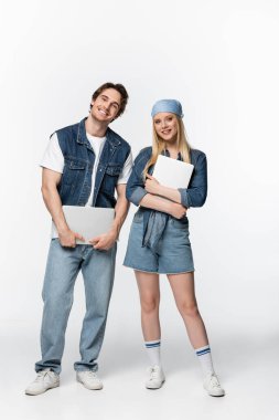 Diz üstü bilgisayarları beyaz kameraya gülümseyen mutlu ve şık bir çiftin tam boy görüntüsü