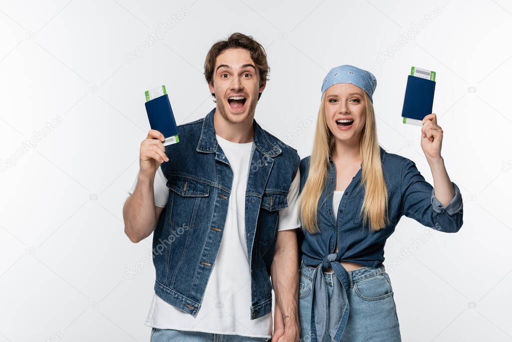 thrilled couple in denim clothes holding hands and travel documents isolated on white