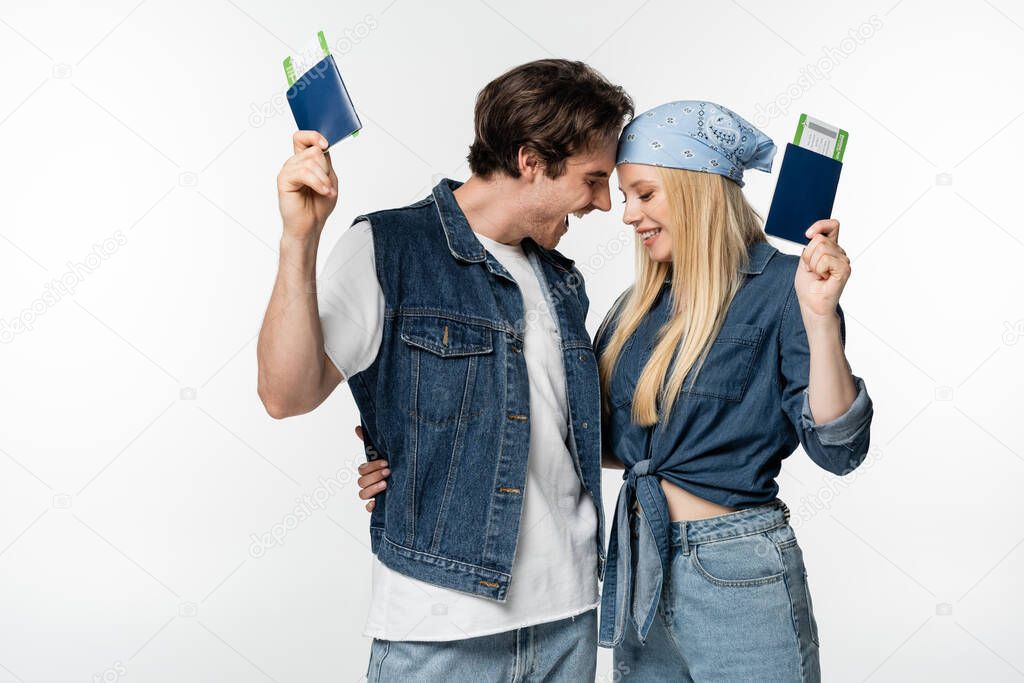 joyful couple in stylish clothes embracing while holding passports with air tickets isolated on white