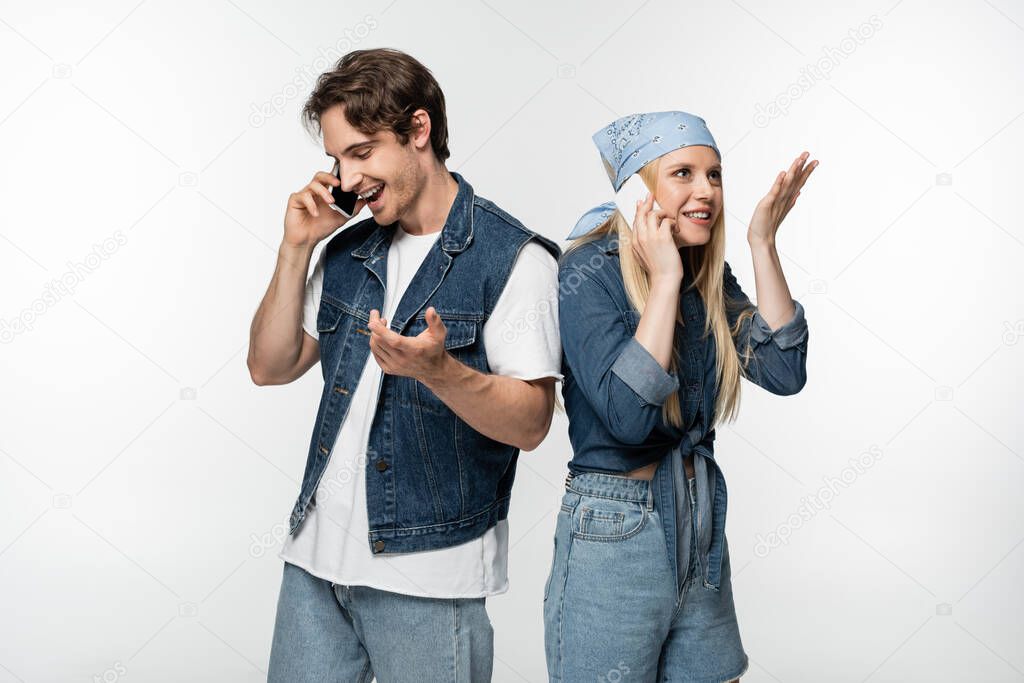 joyful couple in trendy denim clothing talking on mobile phones isolated on white
