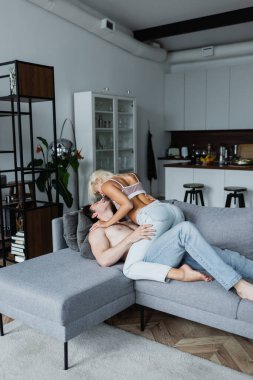 Seksi genç kadın, kanepede üstsüz bir adamı baştan çıkarıyor.