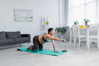 Genç hamile bir kadın spor yaparken dizlerinin üstünde spor yapıyor.