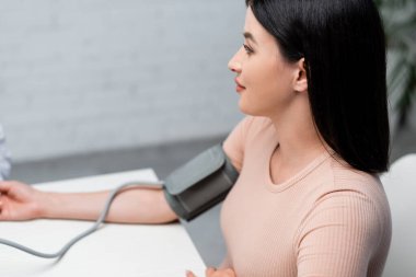 Klinikte tonometreyle kan basıncını ölçen esmer kadın.