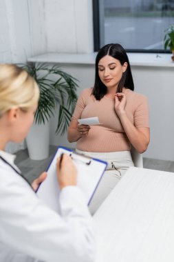 Bulanık doktor, hamile kadının yanındaki panoya reçete yazıyor.