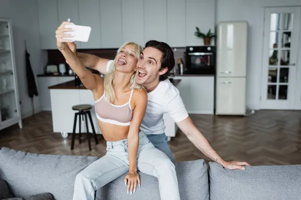 Mujer Feliz Sobresaliendo Lengua Mientras Toma Selfie Con Novio Sala — Foto de Stock