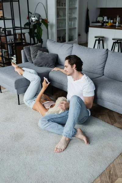 Blonde Woman Showing Smartphone Cheerful Boyfriend Living Room — Stock Photo, Image