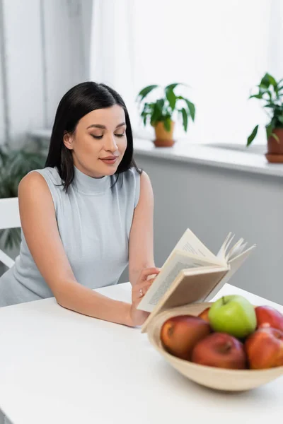 Smiling Woman Reading Novel Fresh Apples Kitchen Table — Stock Photo, Image