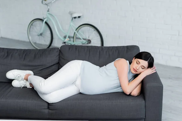 Vista Completa Mujer Embarazada Joven Durmiendo Sofá Cerca Bicicleta Borrosa — Foto de Stock